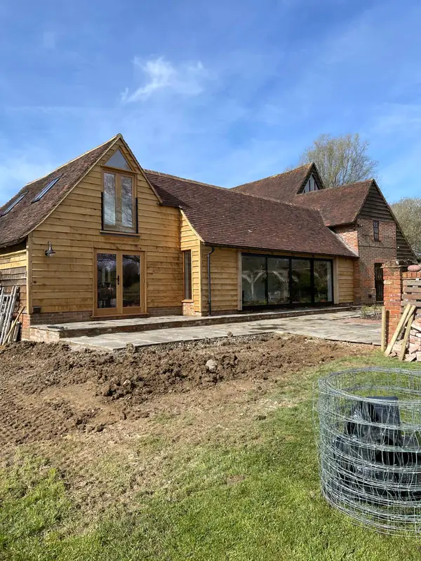 New oak-clad building with a clay tiled roof next to an older brick house, with groundworks still under way