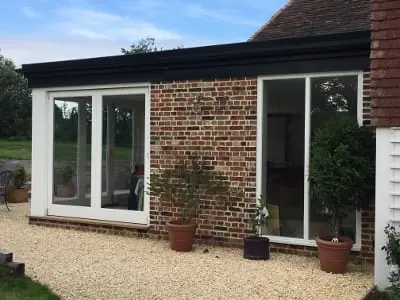 Single storey brick extension with white French doors and potted bay trees
