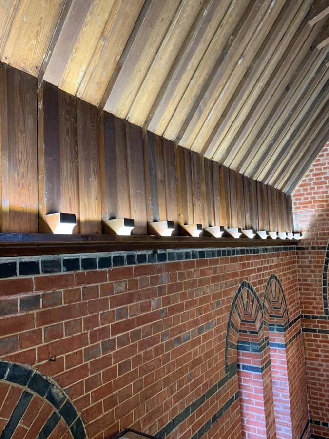 Timber roof boards lit from below along a brick wall