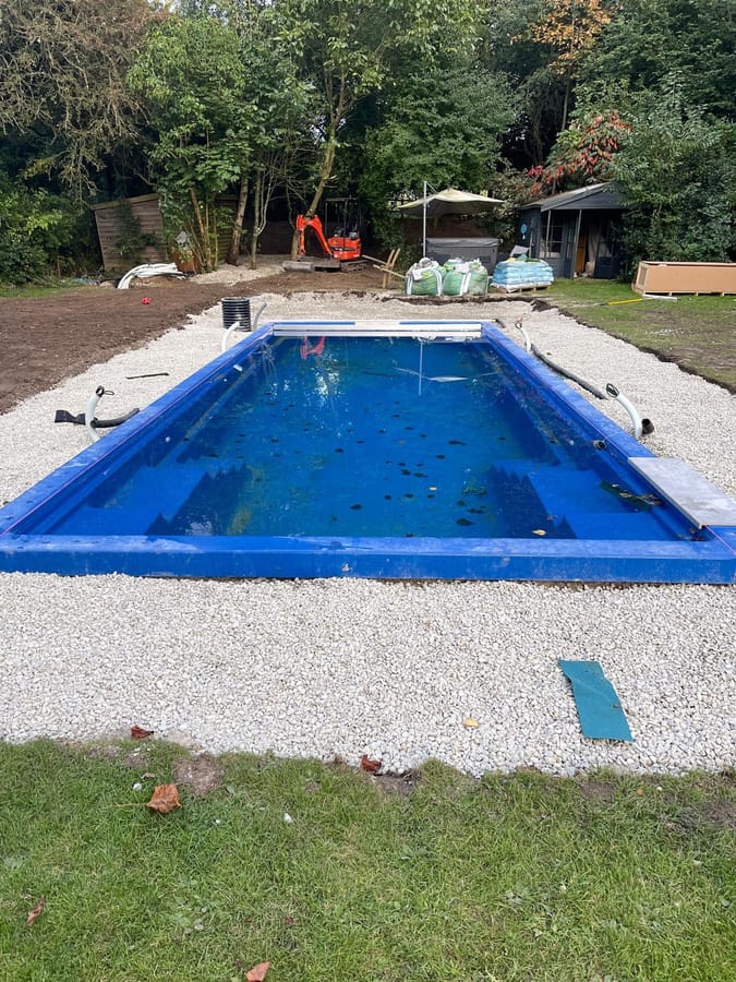 The pool shell set in the ground and surrounded with gravel, before the paving