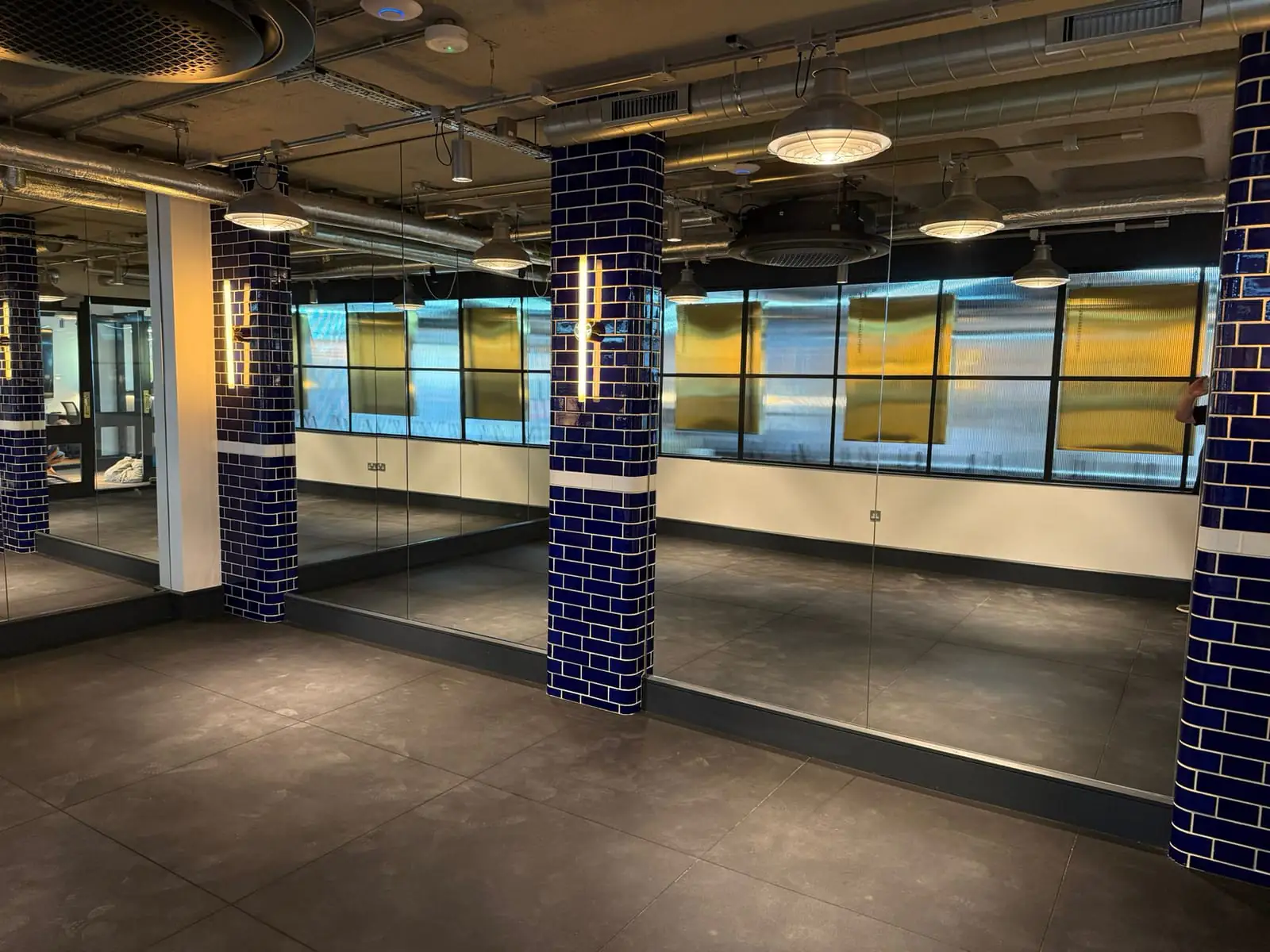 Fitted-out studio with blue tiled columns, mirror walls, industrial pendant lights and exposed ducting