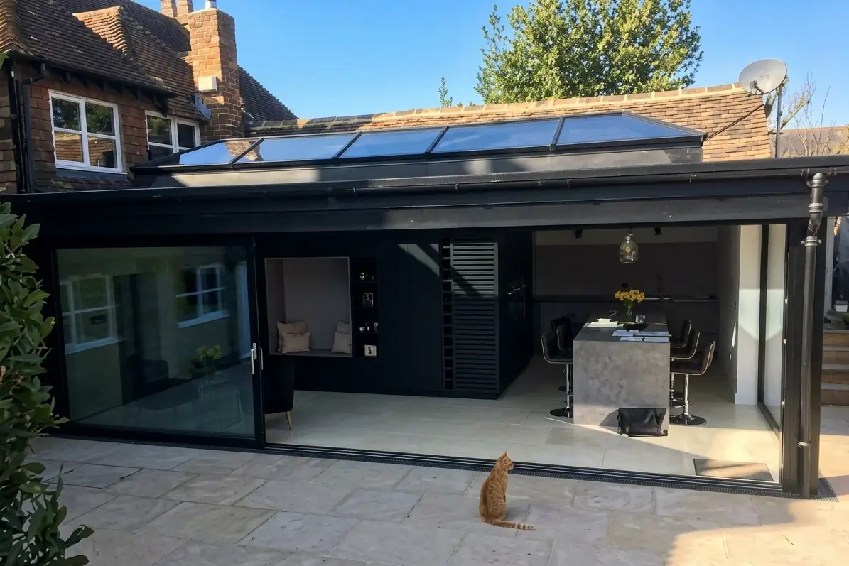 Black-framed glass extension with a roof lantern and sliding doors opening onto a stone terrace