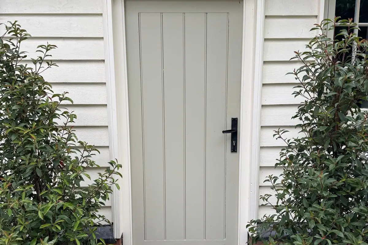 Sage green purpose-made ledged door with a black lever handle, set in white weatherboarding