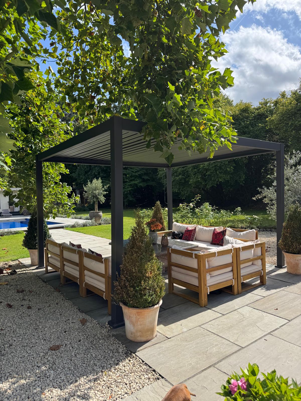 Louvered pergola over a garden seating area beside the pool